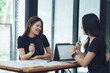 © Kritdanai - Collaborative Success: Two smiling Asian businesswomen engage in a productive meeting, discussing ideas and strategies over laptops and documents.