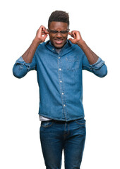 Wall Mural - Young african american man over isolated background covering ears with fingers with annoyed expression for the noise of loud music. Deaf concept.