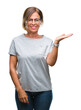 © Krakenimages.com - Middle age senior hispanic woman wearing glasses over isolated background smiling cheerful presenting and pointing with palm of hand looking at the camera.