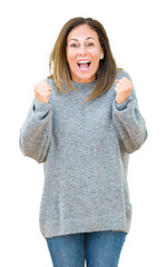 Wall Mural - Beautiful middle age woman wearing winter sweater over isolated background celebrating surprised and amazed for success with arms raised and open eyes. Winner concept.