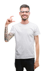 Sticker - Young tattooed adult man smiling and confident gesturing with hand doing size sign with fingers while looking and the camera. Measure concept.