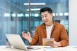 © Liubomir - Asian man mature businessman smiling and engaging in an online meeting while taking notes. He is seated in a modern office setting with a laptop and appears happy and professional.