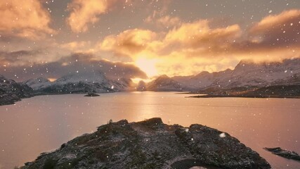 Wall Mural - aerial view from low flying drone of sea, stones, snowy mountains at golden sunset in snowfall in wi