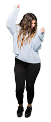 Wall Mural - Young beautiful woman wearing winter sweater very happy and excited doing winner gesture with arms raised, smiling and screaming for success. Celebration concept.