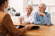 © New Africa - Pension plan. Senior couple consulting with insurance agent at wooden table indoors