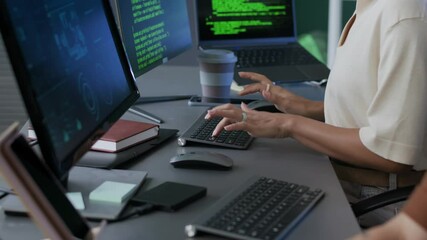 Tilt up shot of male programmers hands typing on laptop and his female colleague working on program coding on PC in evening office