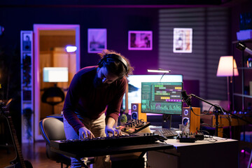 Leinwandbilder - Cheerful artist playing music on electronic keyboard in home studio, recording new songs and having fun with audio session. Confident musician plays tunes on piano midi controller.