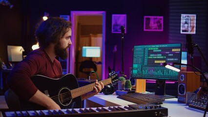 Fototapete - Music producer mixing guitar sounds played by him on acoustic instrument, using electronic soundboard console and daw software. Skilled musician developing new tunes, home studio. Camera B.