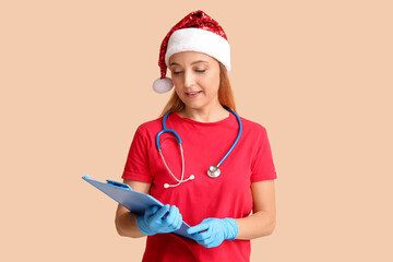 Wall Mural - Mature female doctor in Santa hat with clipboard on beige background