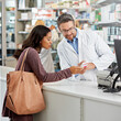 © peopleimages.com - Drugstore, pharmacist and helping woman by counter for pills side effects, prescription drugs dosage and advice. Dispensary, mature man or customer service in pharmacy with medication box information