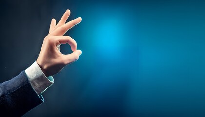 A hand in a business suit makes the okay sign against a blue backdrop. Represents approval, agreement, and positive feedback.