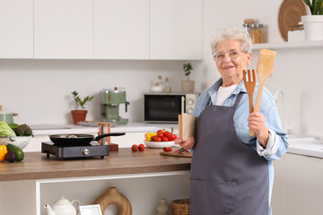 Wall Mural - Senior woman with spatulas and recipe book frying food in kitchen