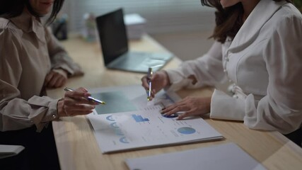 Wall Mural - Two women are sitting at a table with papers and a laptop. They are discussing something important. Scene is serious and focused