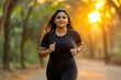 © PRASANNAPIX - a Indian fat plus size smiling woman, wearing sport wear, running at garden, clear day light