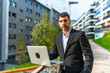 © unai - Confident businessman using laptop standing in the city