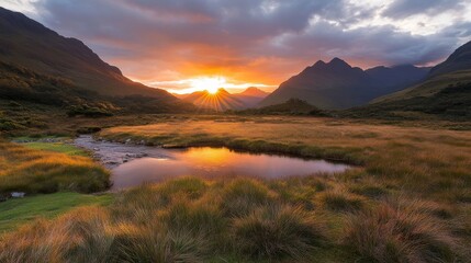Poster - Golden light from the sunset enhances the tranquil grassy field, while dramatic clouds and mountains create a peaceful atmosphere by the rippling stream