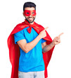 © Krakenimages.com - Young handsome man with beard wearing super hero costume smiling and looking at the camera pointing with two hands and fingers to the side.