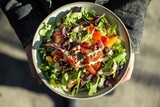 Top-down view of a colorful salad bowl with fresh vegetables, greens, and sesame seeds drizzled with creamy dressing
