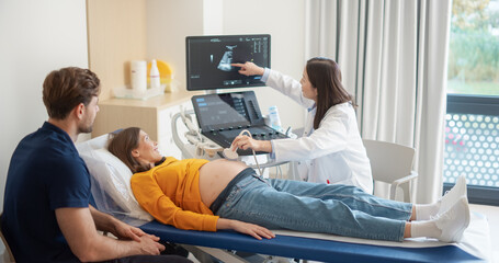 Aufkleber - Caring Female Hospital Obstetrician Conducting an Ultrasound Exam for a Pregnant Woman. Young Couple Watching the Screen while Asian Doctor Describes the Baby’s Growth to Expectant Mother