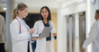 © Gorodenkoff - Diverse Healthcare Workers Walking Through a Modern Hospital Hall with a Laptop Computer. Caucasian Female Doctor and Asian Physician Discussing Patient Treatment Options on the Move