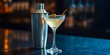 © DeeDay - A refreshing cocktail garnished with an olive in a martini glass, next to a cocktail shaker on a dark bar top