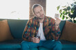 © deagreez - Young man in casual plaid shirt relaxing on sofa with a thoughtful expression at home