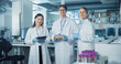 © Gorodenkoff - Portrait of a Diverse Research Team Standing in a Modern Laboratory in White Coats, Looking at Camera and Smiling. Female and Male Scientists Hold Test Samples and Tablet Computer