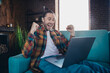 © deagreez - Happy young man with a beard celebrates success while sitting in a stylish living room. The energetic guy is in a plaid shirt