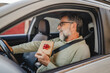 © Miljan Živković - Senior mature man sit in the car and hold small gift with red ribbon