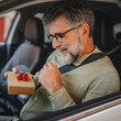 © Miljan Živković - Senior mature man sit in the car and hold small gift with red ribbon