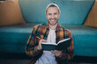 © deagreez - Young male reading in a cozy living room, smiling and enjoying a peaceful leisure day indoors