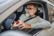 © Miljan Živković - Senior mature man sit in the car and hold small gift with red ribbon