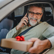 © Miljan Živković - Senior mature man sit in the car hold gift box and have a phone call