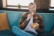 © deagreez - Young man enjoying a relaxing day at home while sitting on a cozy sofa with a bowl of chips in a modern and stylish loft living room.