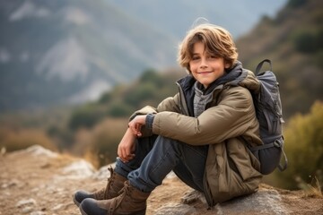 Wall Mural - Portrait of a boy with backpack sitting on a rock in the mountains