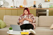 © Bliss - Young plus size woman sits comfortably on the couch engaged with her smartphone in a warm home.