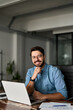 © insta_photos - Vertical portrait of smiling young business man startup founder, happy Latin entrepreneur, confident business owner looking at camera using laptop computer technology working at corporate office desk.