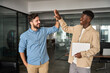 © insta_photos - Two diverse happy professional young men teammates giving high five celebrating business triumph, corporate startup project success, good team partnership teamwork result together at work in office.