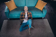 © deagreez - Relaxed young man with brown hair smiling on a cozy living room floor during a sunny weekend indoors, wearing a trendy checkered shirt