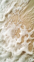Poster - Soft white sea foam gently washes over golden sand on a sunny beach, creating a beautiful natural texture perfect for backgrounds and designs related to summer, relaxation, and travel