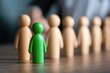 © Design Depot - An individual green figure leads a sequence of wooden figures, embodying concepts of leadership, guidance, and standing out within a group of similar entities.