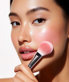 Young beautiful Asian woman applying pink blush on her skin with brush