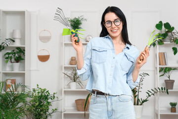 Wall Mural - Beautiful young woman with gardening tools and houseplants at home