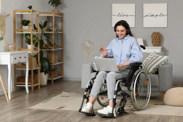 Wall Mural - Young woman in wheelchair with headphones using laptop at home