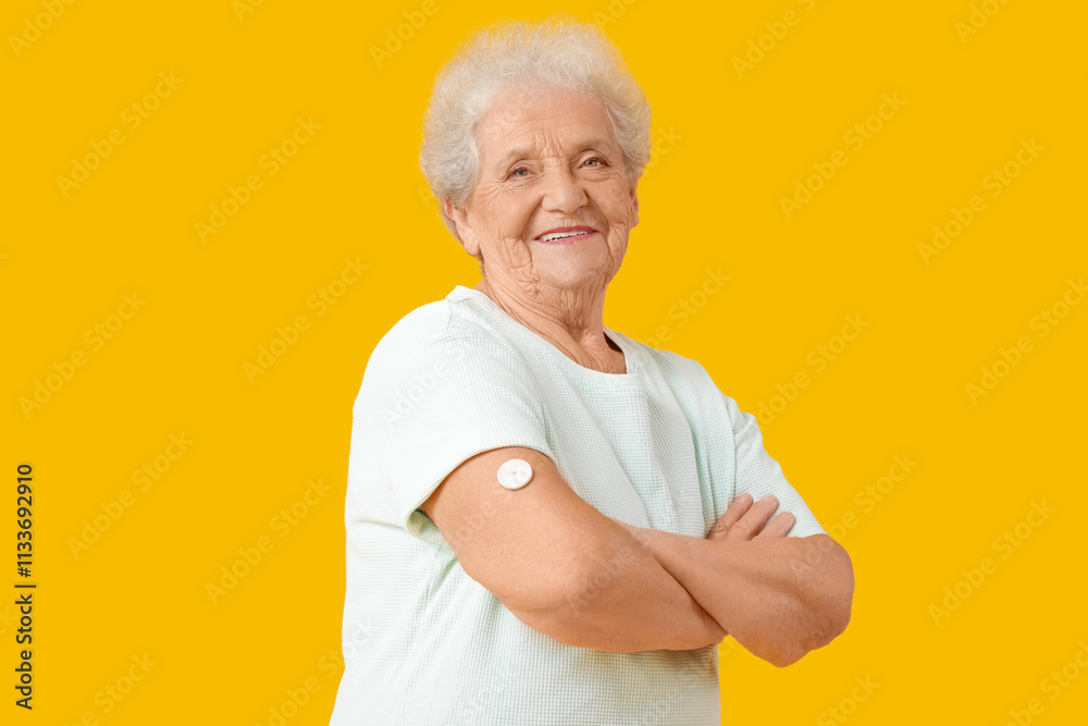 Diabetic senior woman with glucose sensor on yellow background