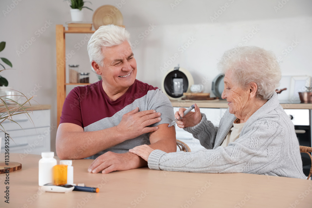 Diabetic senior man with his wife using lancet pen in kitchen
