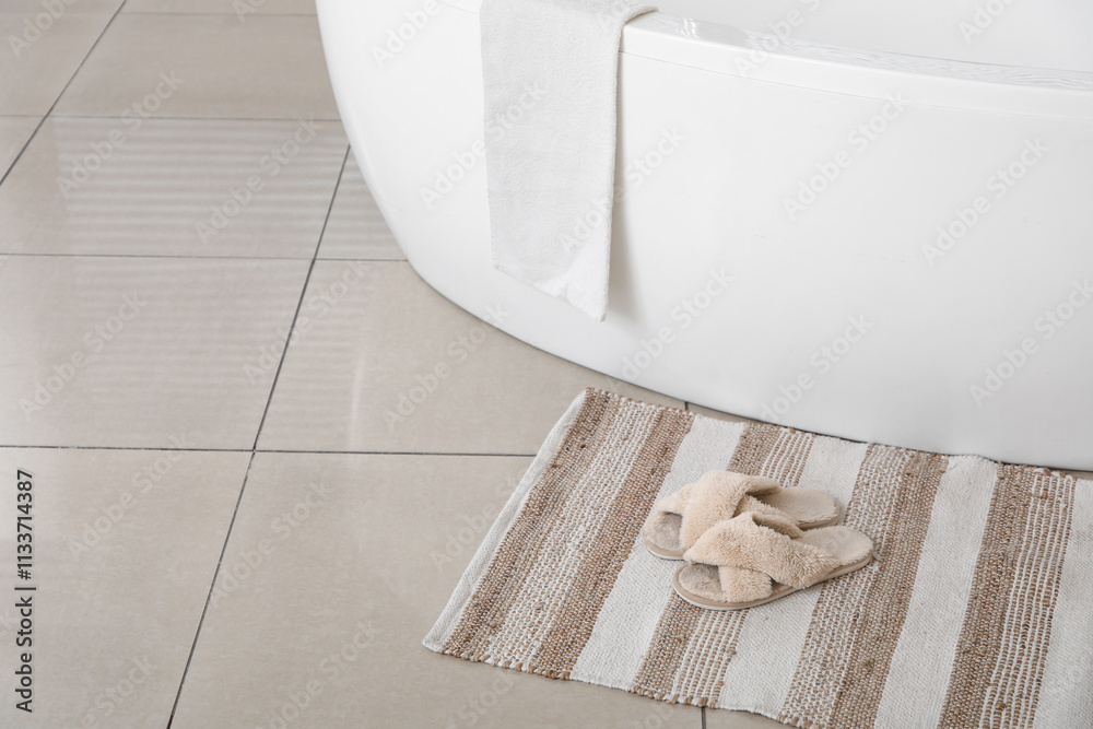 Soft slippers on rug near modern bathtub in bathroom
