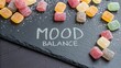 © Justlight - A cascading view of assorted gummy vitamins in playful soft pastel colors contrasting against a dark slate backdrop. A few gummies are turned to display the Mood Balance
