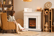 © Pixel-Shot - Young woman sitting in armchair near fireplace at home