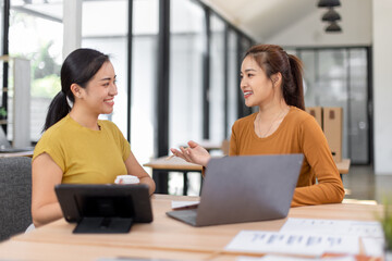 Wall Mural - Happy two asian female freelance entrepreneurs reading and planning analyzing the financial report, business plan investment,  on computer while working together in the office.
